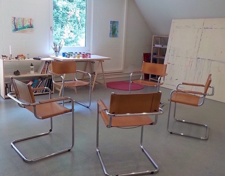 Heller Atelierraum mit Malwand, Tisch mit Farben und Stühlen